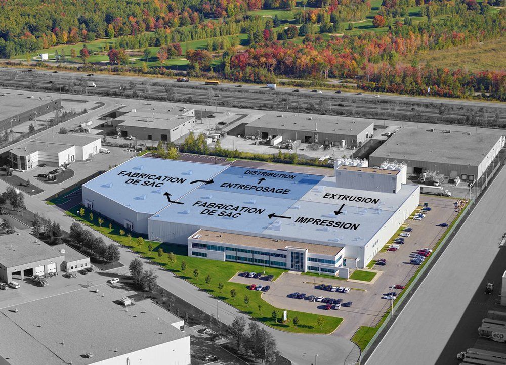 Aerial view of a large industrial building with process labels, surrounded by smaller buildings and trees.