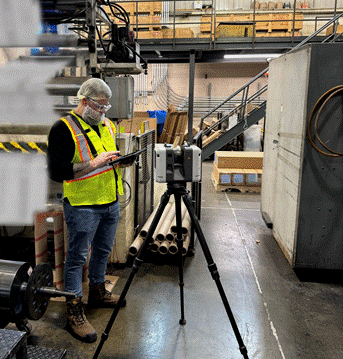 Homme avec une veste jaune tenant un iPad à côté d'un capteur laser Lidar dans une usine 
