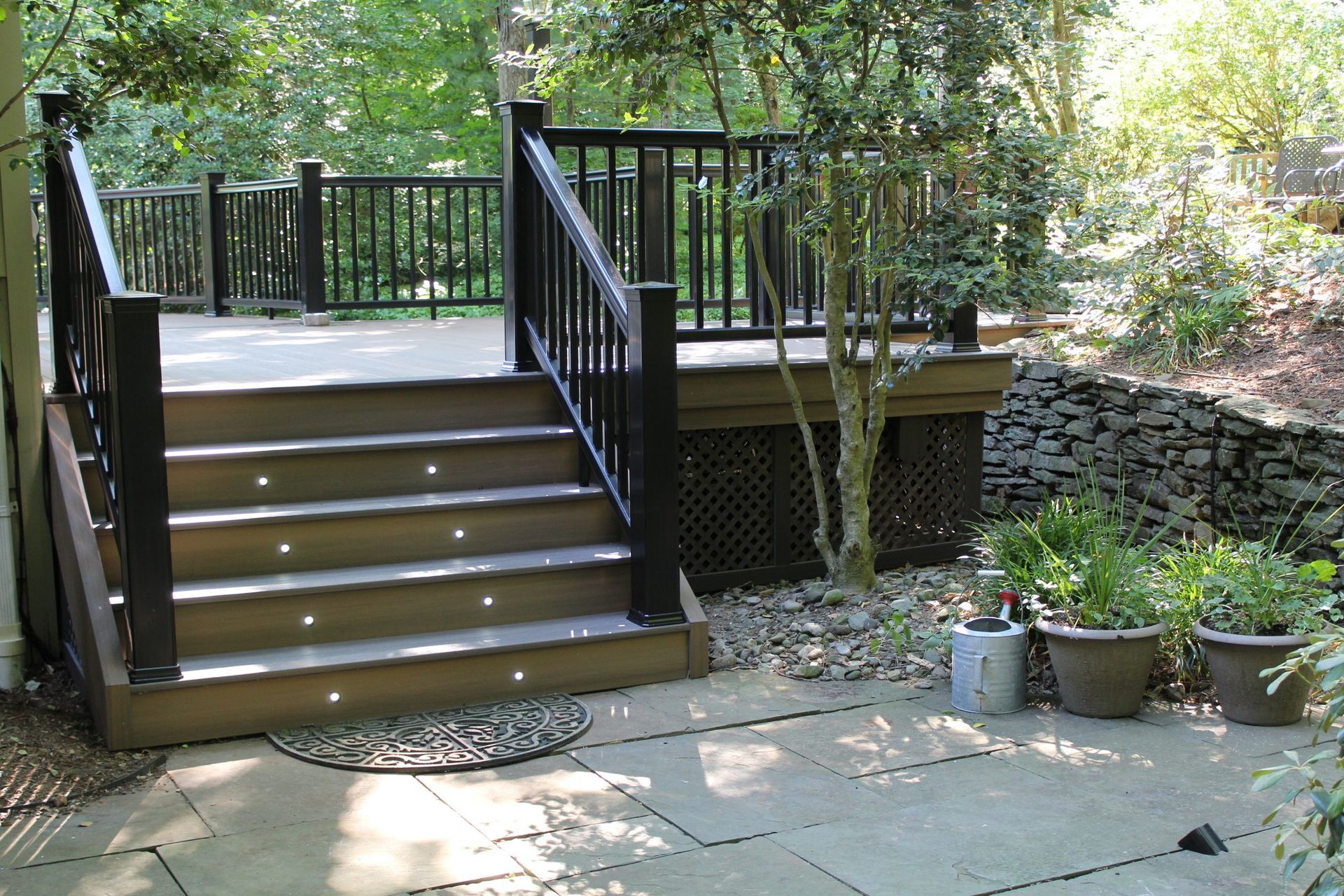 Deck stairs with LED lighting and black railings leading to landscaped patio by New Dimensions