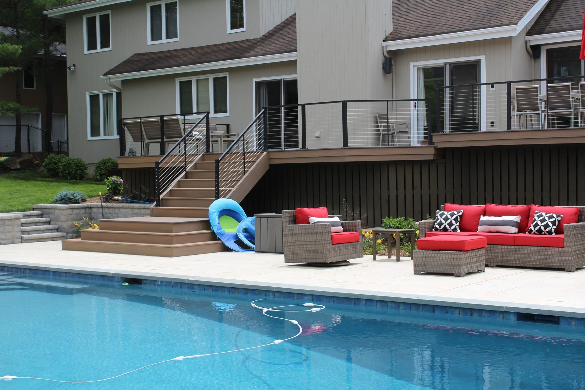 Poolside deck with cable railings and brown stairs featuring outdoor seating by New Dimensions