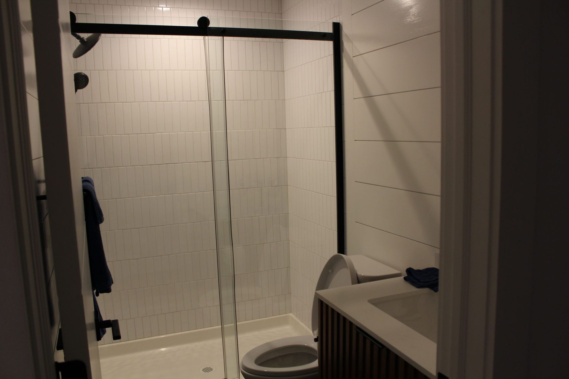 Modern bathroom with glass shower and white vertical tile walls featuring black fixtures.