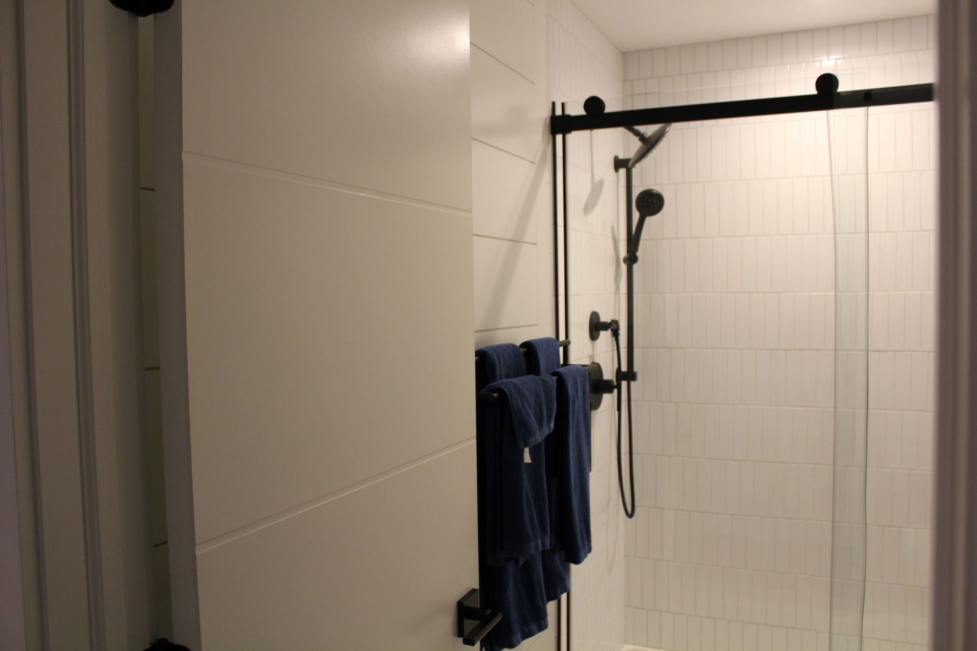 Bathroom shower with black framed glass doors, white tile walls, and matching black towel rack.