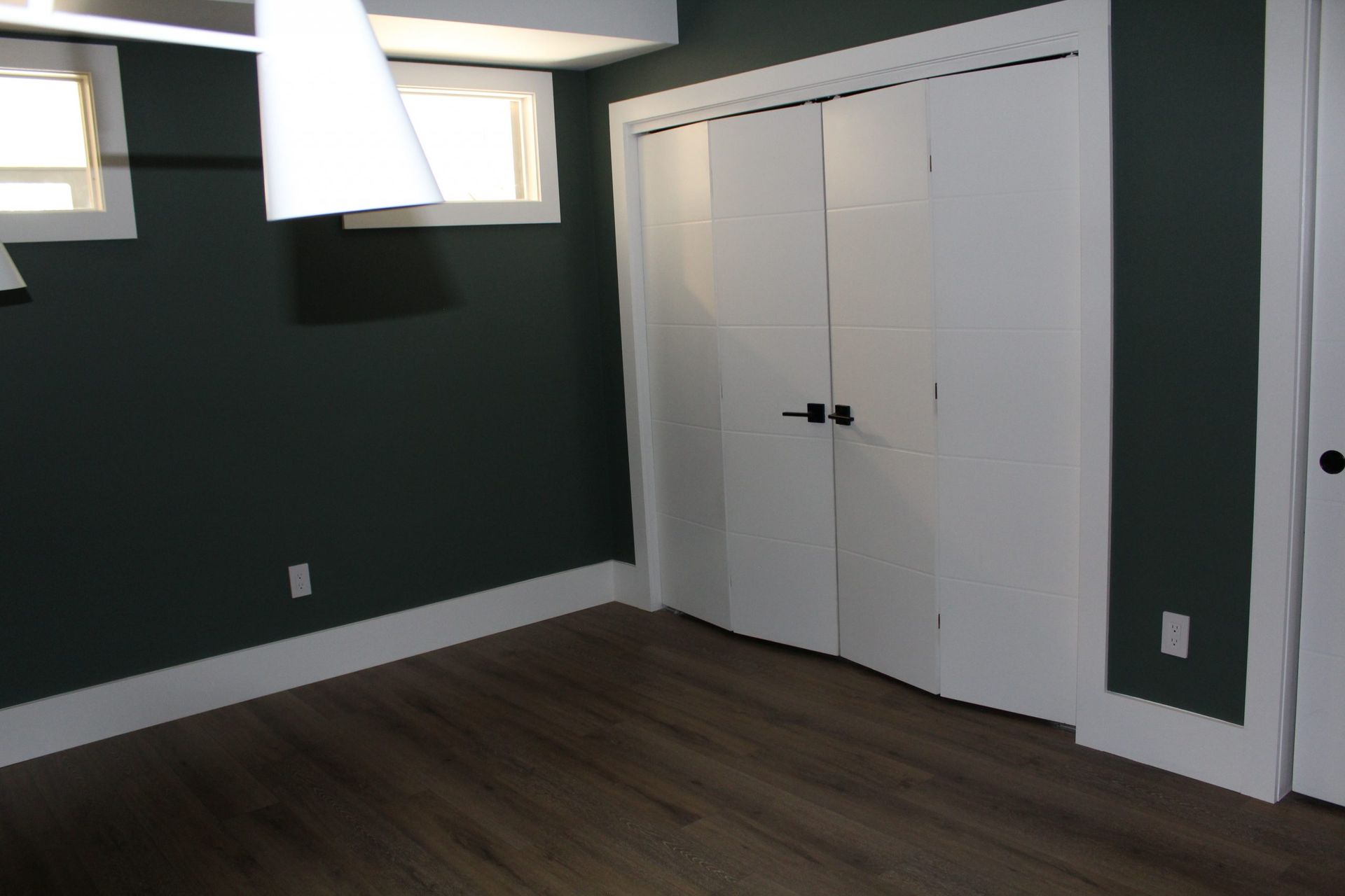 Bedroom with dark green accent wall, white closet doors, and wooden flooring.