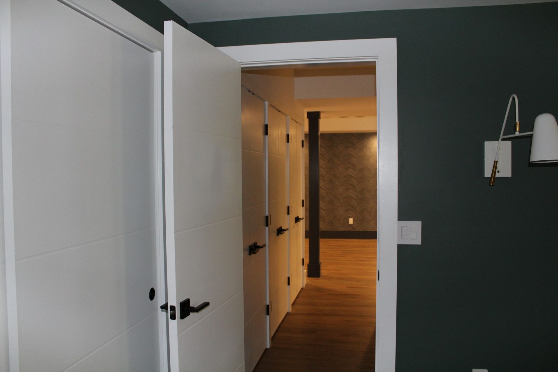 Hallway view from bedroom featuring white paneled doors, dark handles, and wooden flooring.