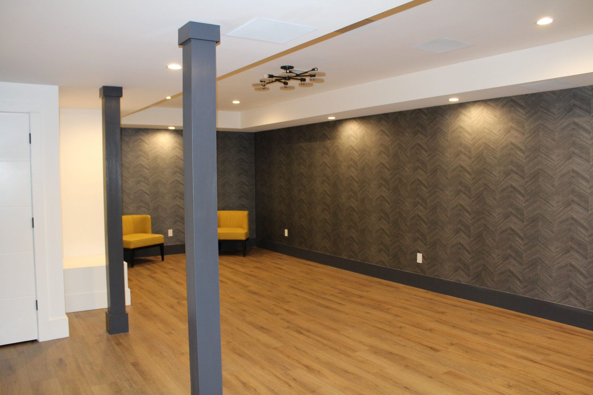 Spacious living area with wood flooring, dark accent wallpaper, and recessed lighting.