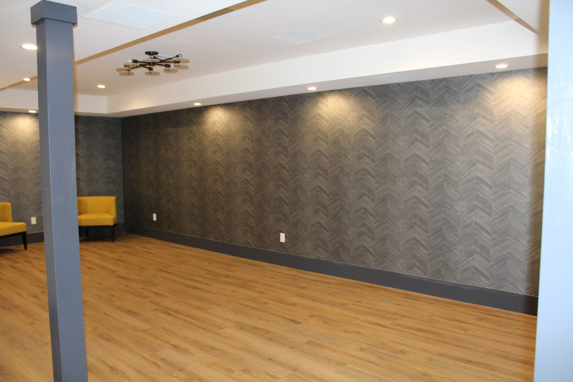 Large open room with chevron-patterned accent wall, wood flooring, and yellow accent chairs.