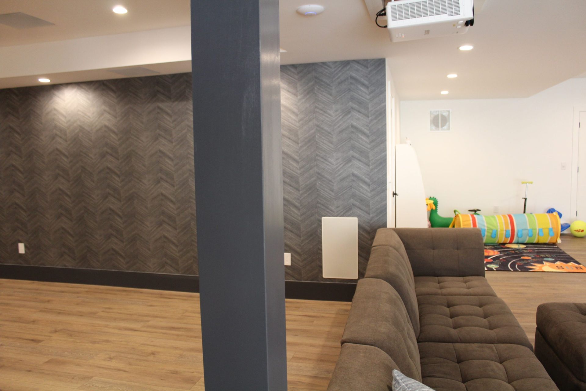 Modern basement with dark patterned walls, gray sofa, and play area with colorful toys.
