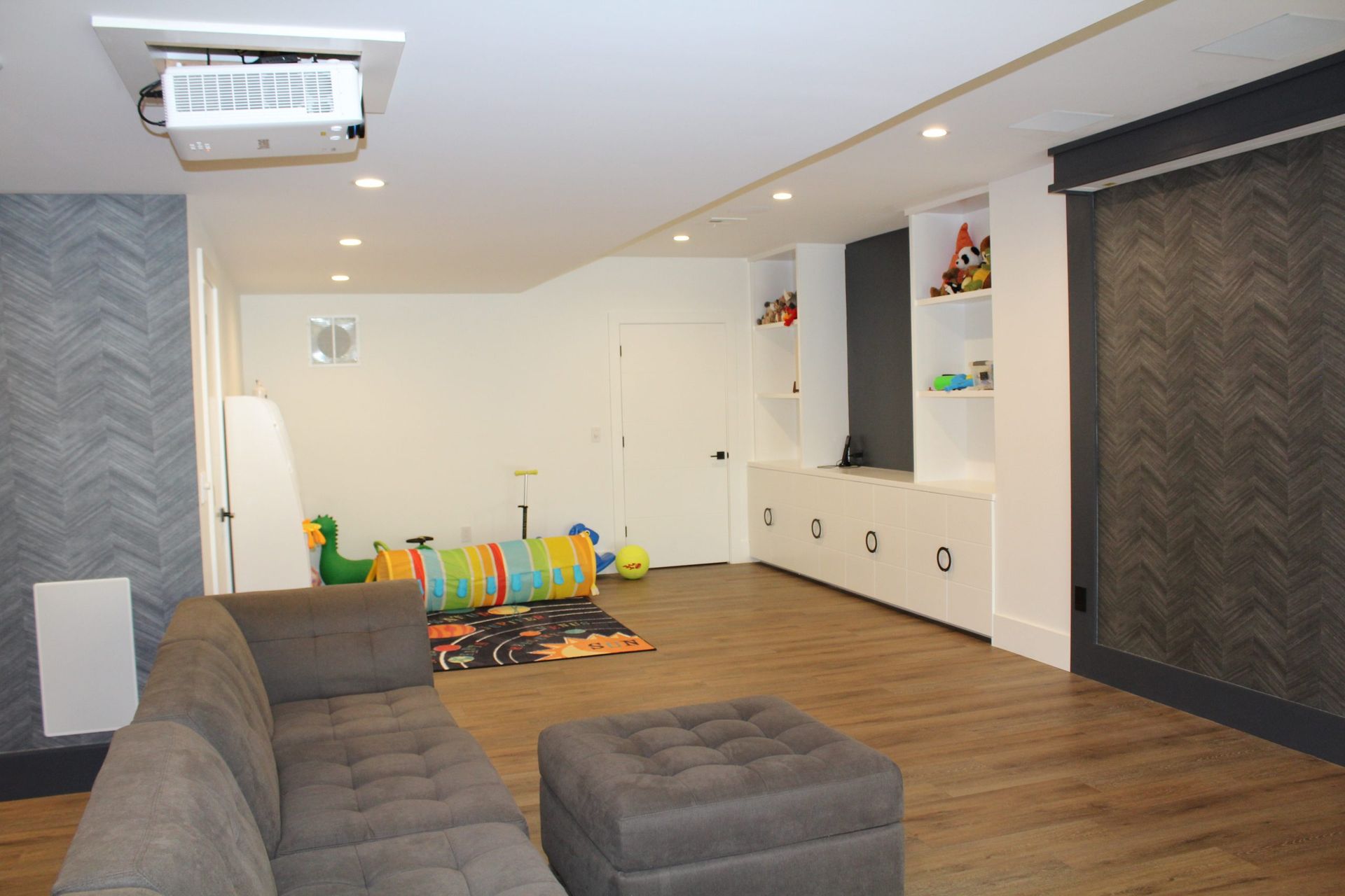 Open basement design with gray walls, recessed lighting, projector, and white storage cabinets.