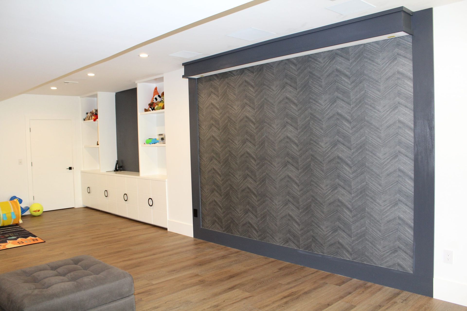 Modern entertainment room with built-in shelving, gray accent wall, and wooden flooring.