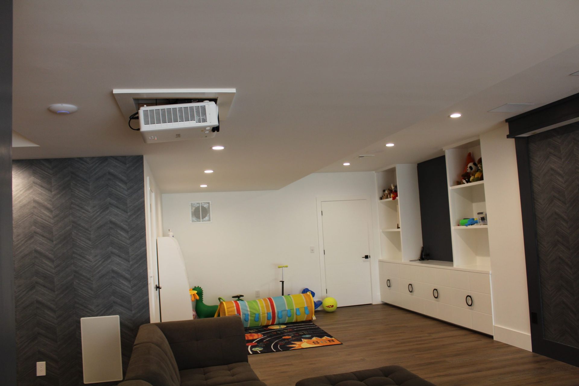 Basement play area featuring toys, built-in shelves, and a mounted projector on the ceiling.