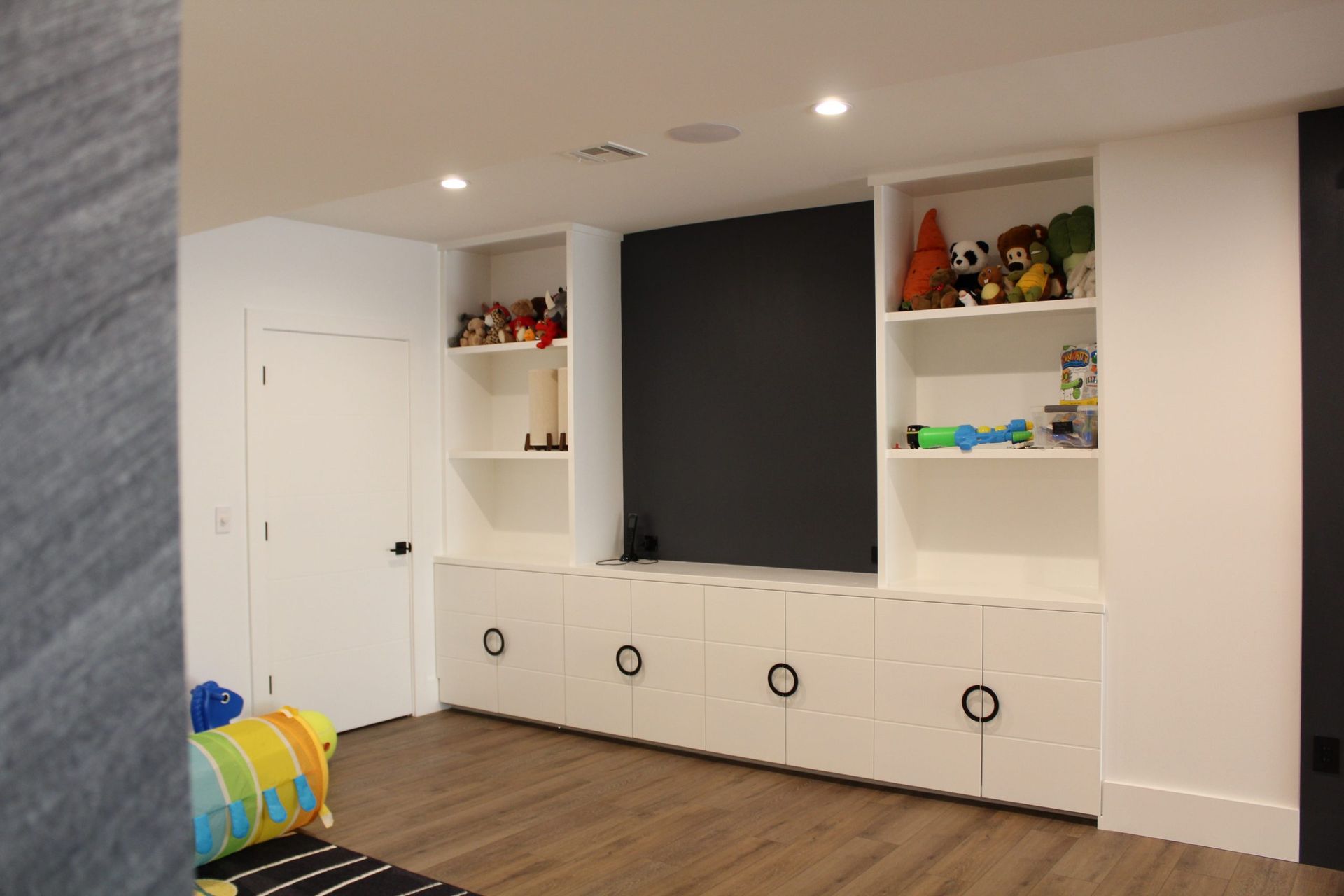 White built-in storage shelves filled with toys and games in a children’s playroom.