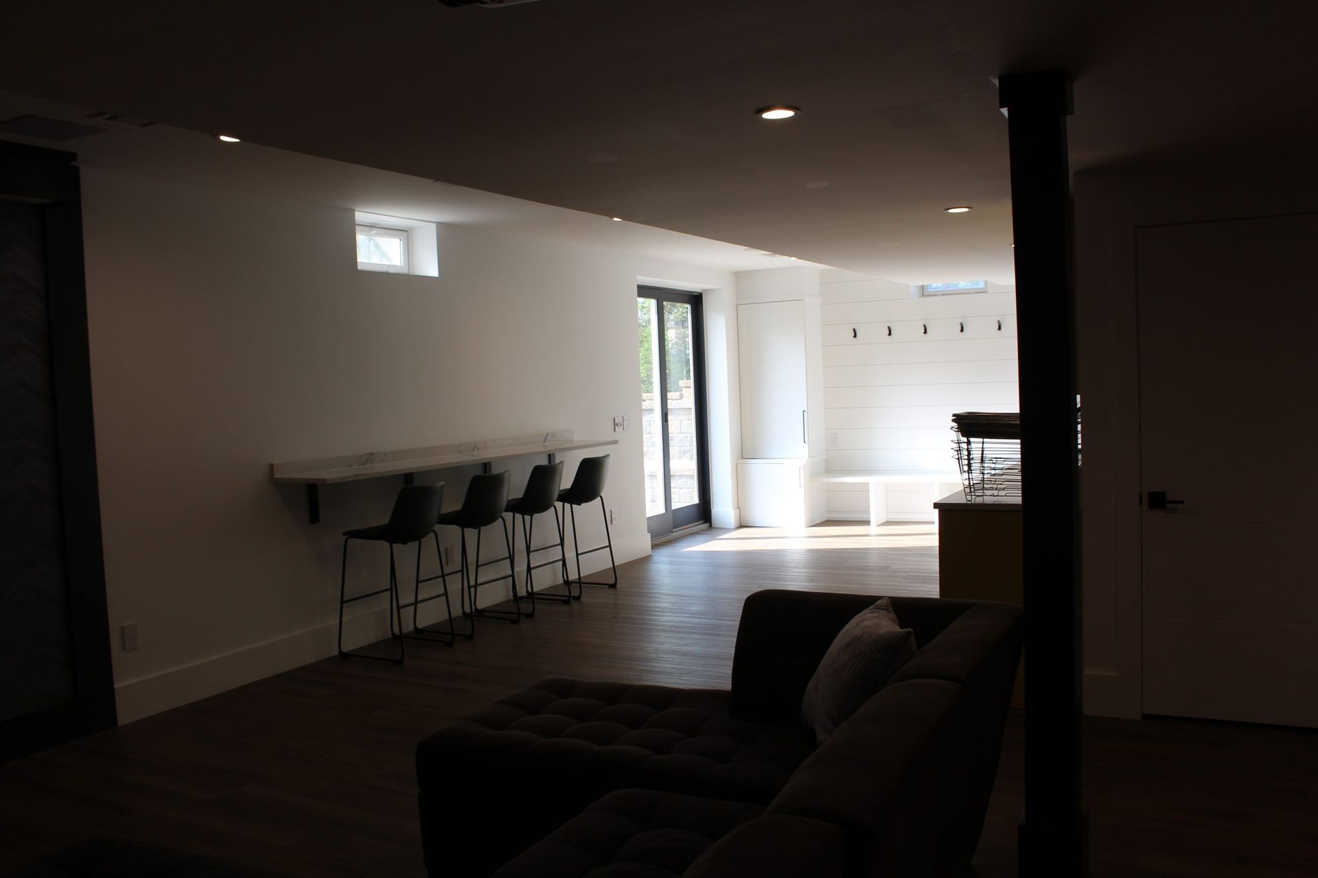 Modern basement seating area with sectional couch and bright window lighting.