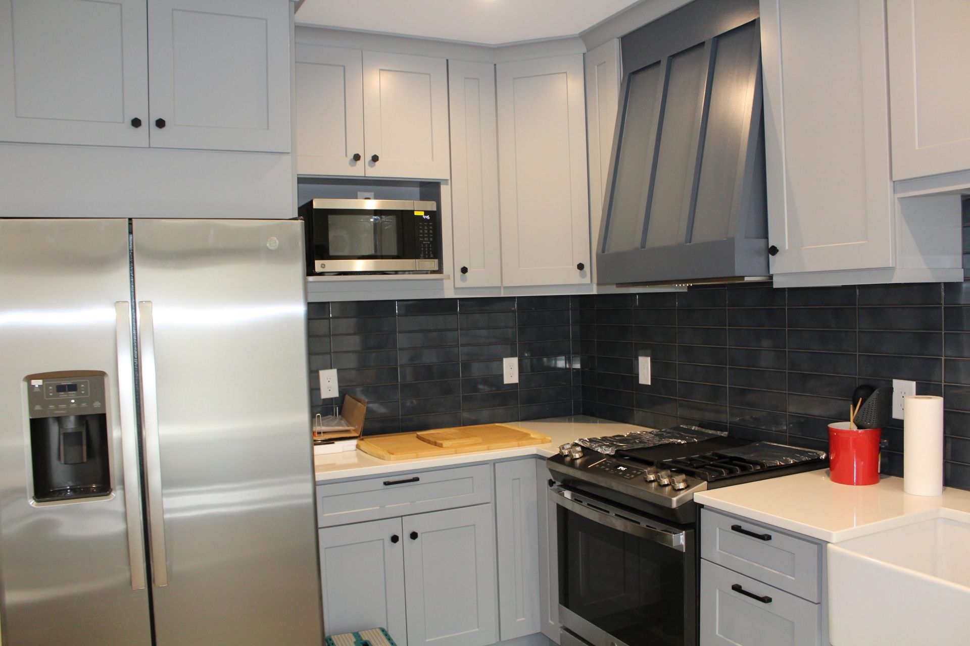 A gray kitchen with stainless steel appliances, light blue cabinets, and a dark blue tiled backsplash.