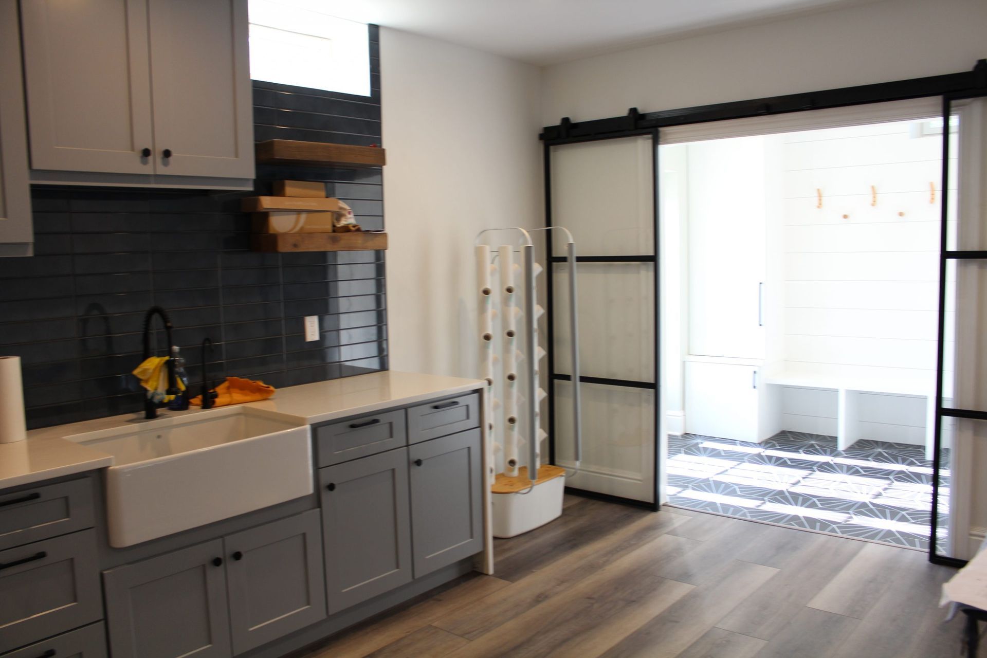 A modern kitchen with gray cabinets, a white farmhouse sink, and a sliding glass door leading to a patio.