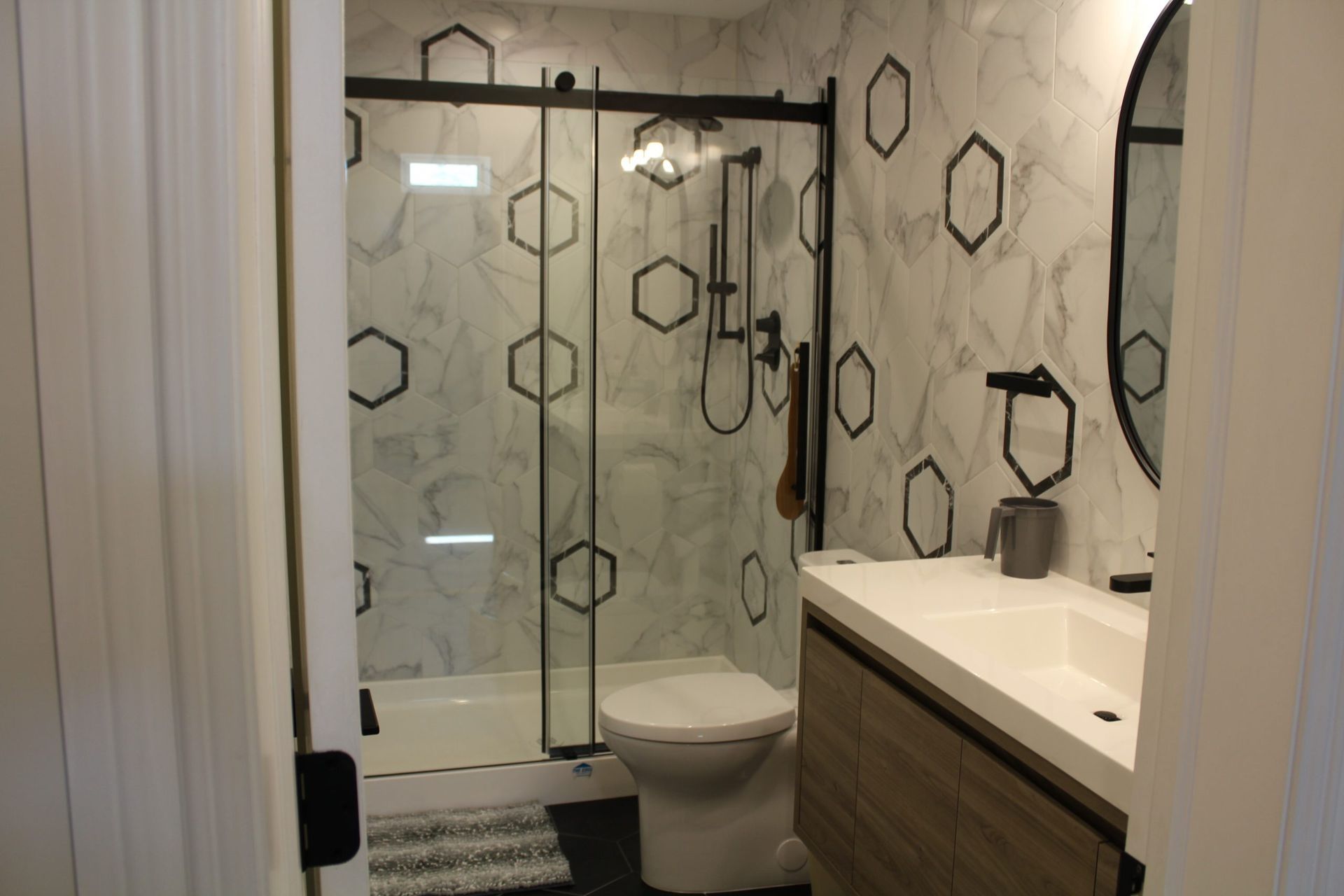 Modern bathroom with a patterned accent wall, glass shower, toilet, and wood-tone vanity.