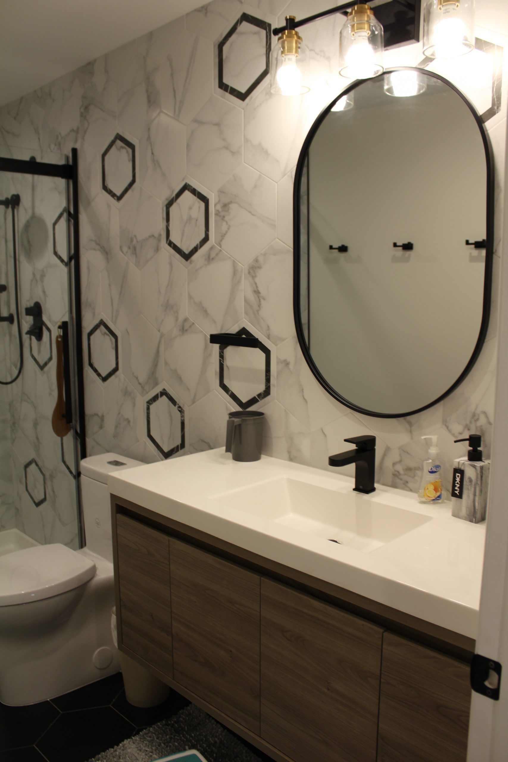 Modern bathroom with white marble-look hexagon tile accent wall, vanity with black faucet.