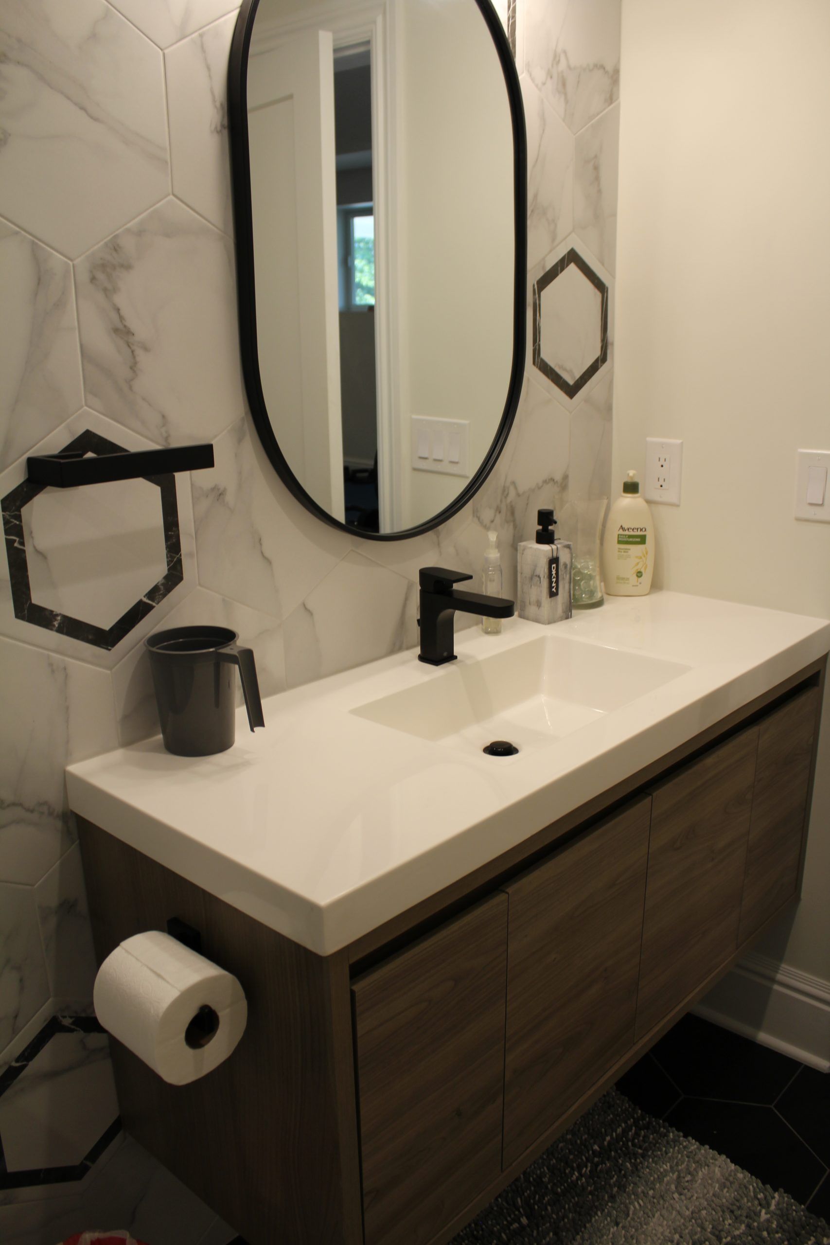 Modern bathroom with floating wood vanity, white countertop, black faucet, and oval mirror.