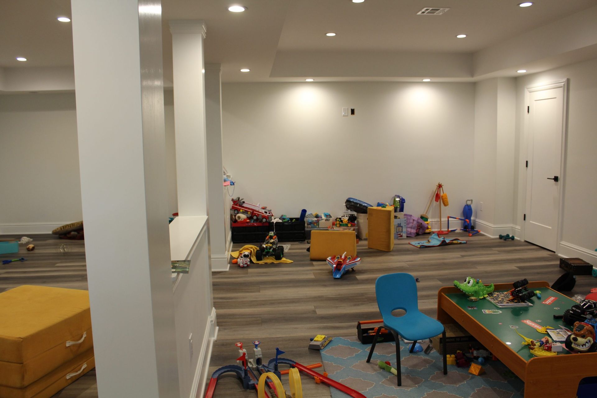 A playroom with toys scattered on the floor, along with furniture and support columns.
