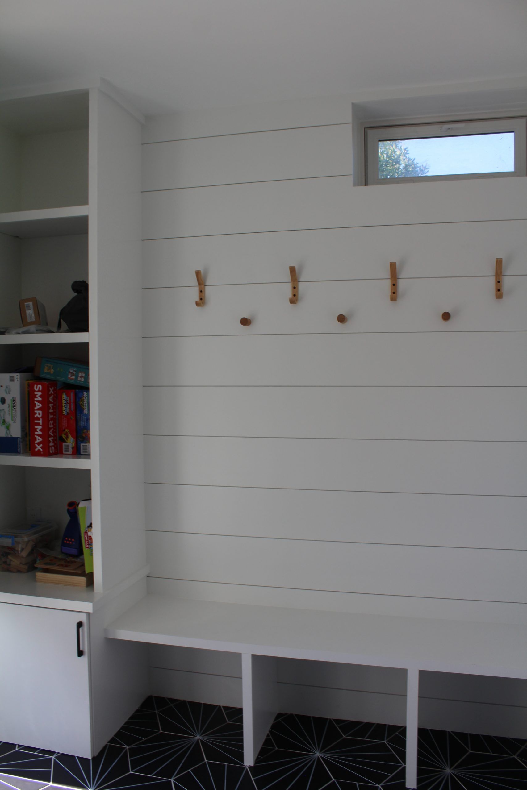 A room with a bench , shelves , hooks and a window.