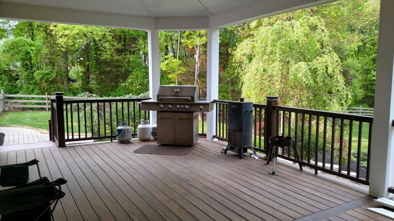 There is a grill on the deck with a view of the woods.