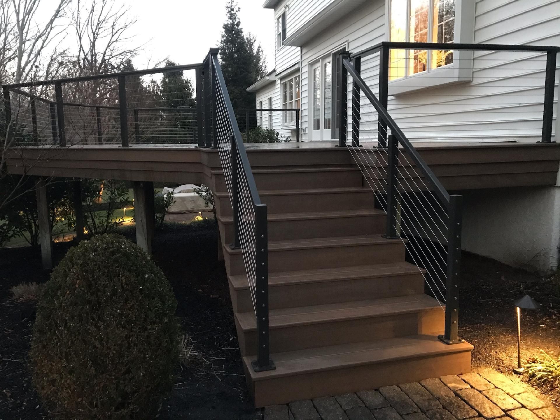 Brown composite deck with black cable railings and stairs, featuring evening lighting.