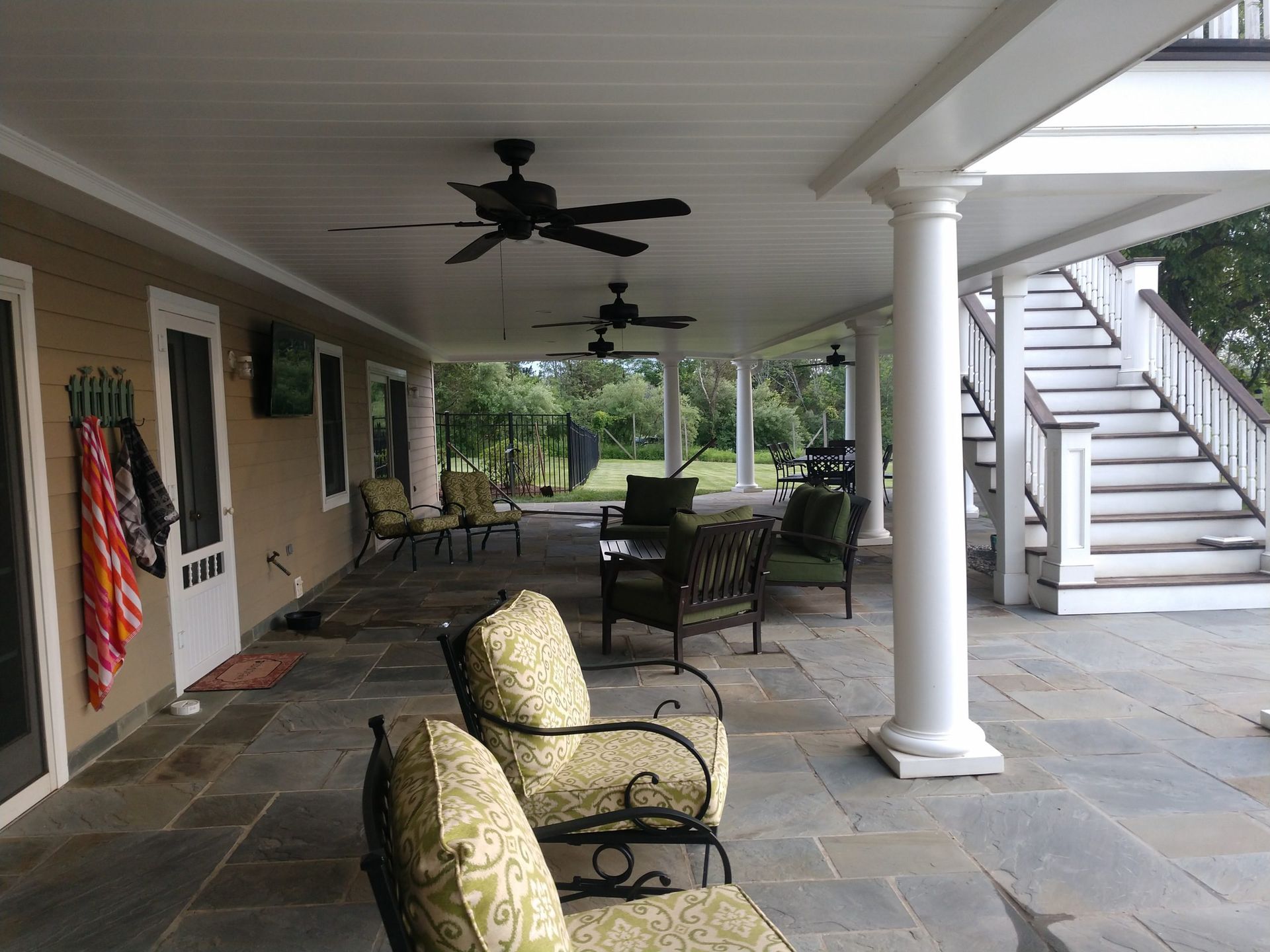 Covered under-deck lounge with white columns, ceiling fans, and stone flooring.