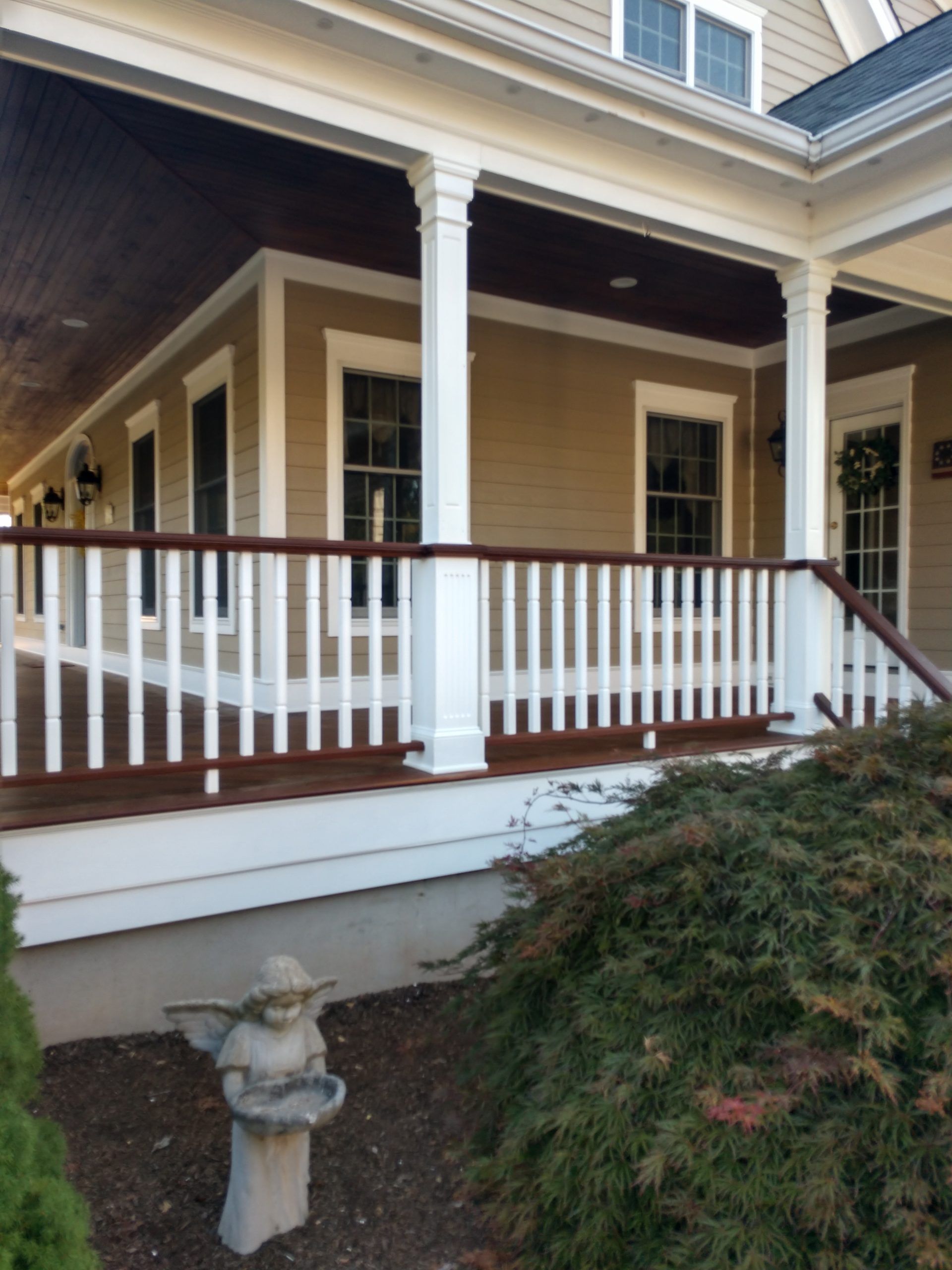 Close-up of front porch with white railings, wooden ceiling, and small garden statue beneath.