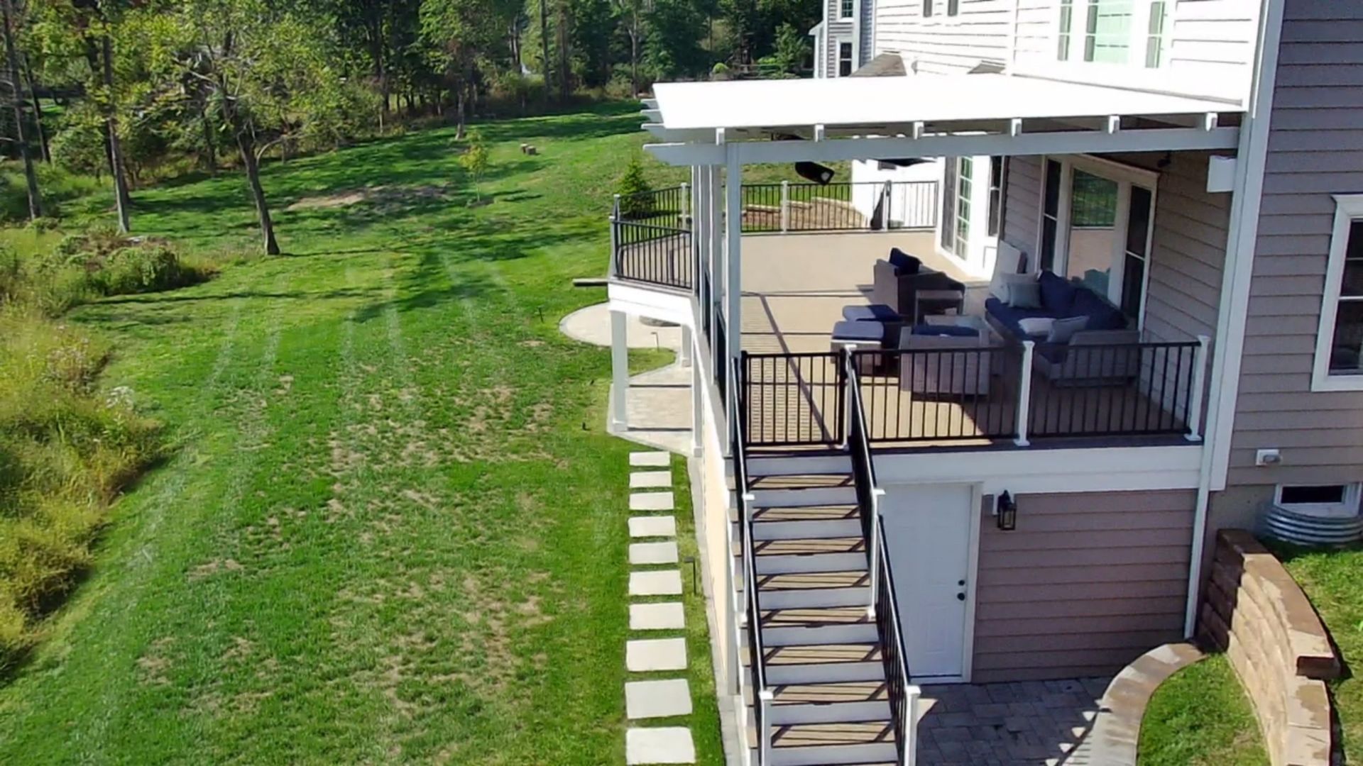 Raised deck with stairs, covered seating area, and black railing overlooking spacious green lawn.