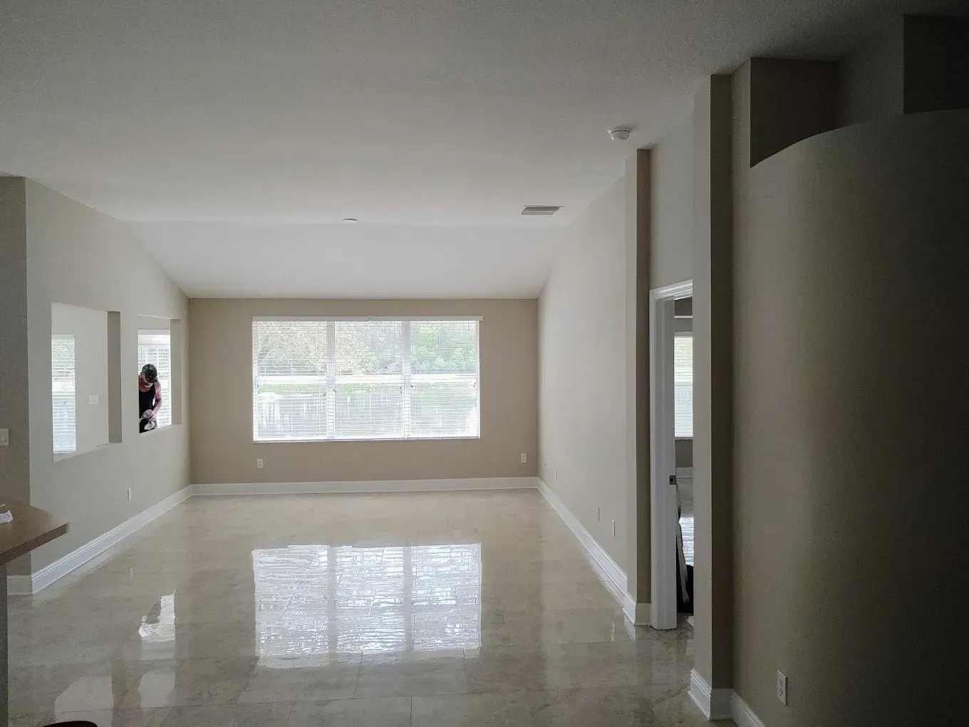 Empty living room with light-colored walls, large window, and shiny tile flooring.