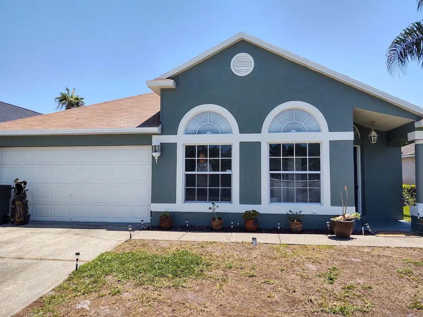 Blue house with white trim, arched windows, and a brown roof under a clear blue sky.