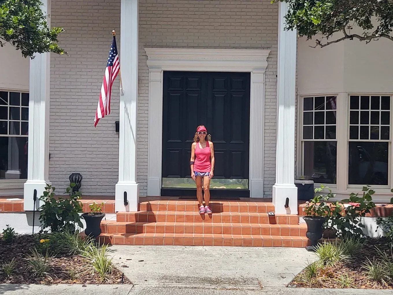 Woman in athletic wear stands on steps of white building with American flag.
