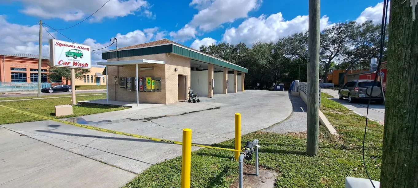 Car wash with beige building, green roof, and several bays. Blue sky and trees in background.
