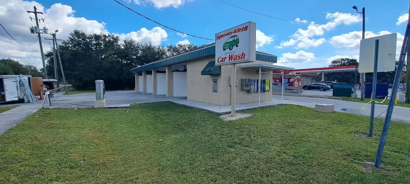 Exterior view of a car wash with a green sign and several bays, set against a blue sky.