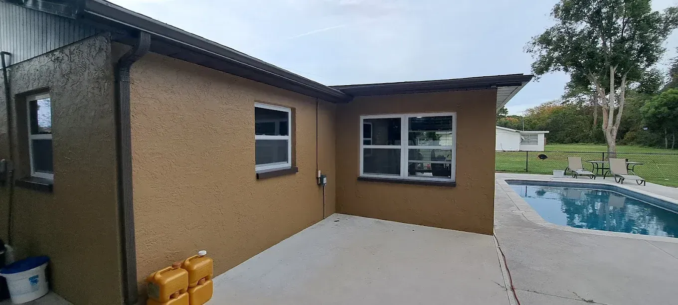 Tan-colored house with windows, gray patio, and a swimming pool in the backyard.