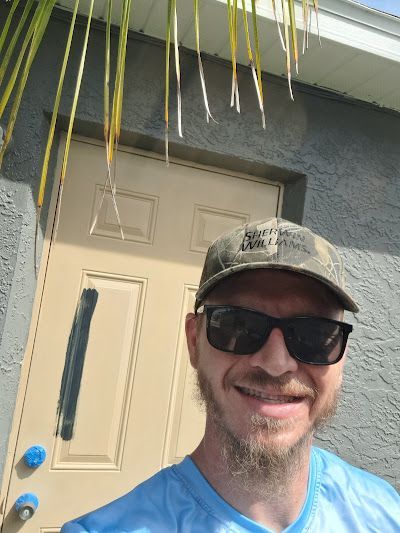 Man wearing sunglasses and hat, standing in front of a tan door.
