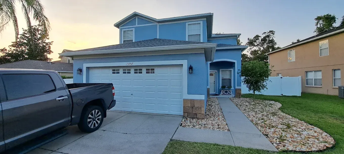 Blue two-story house with a gray pickup truck parked in the driveway. The house has a white garage door.