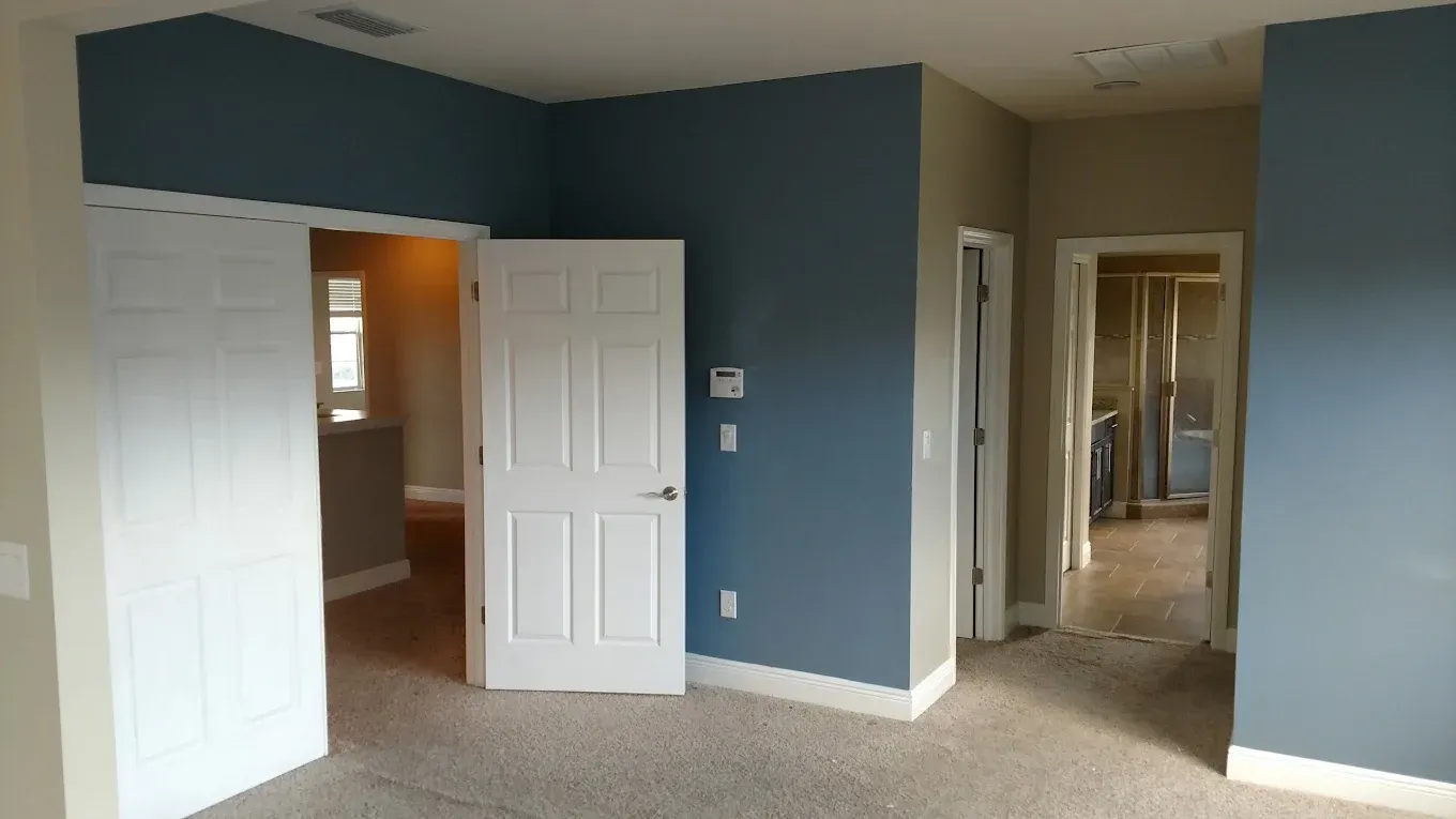 Empty bedroom with blue accent walls, white doors, and beige carpet.
