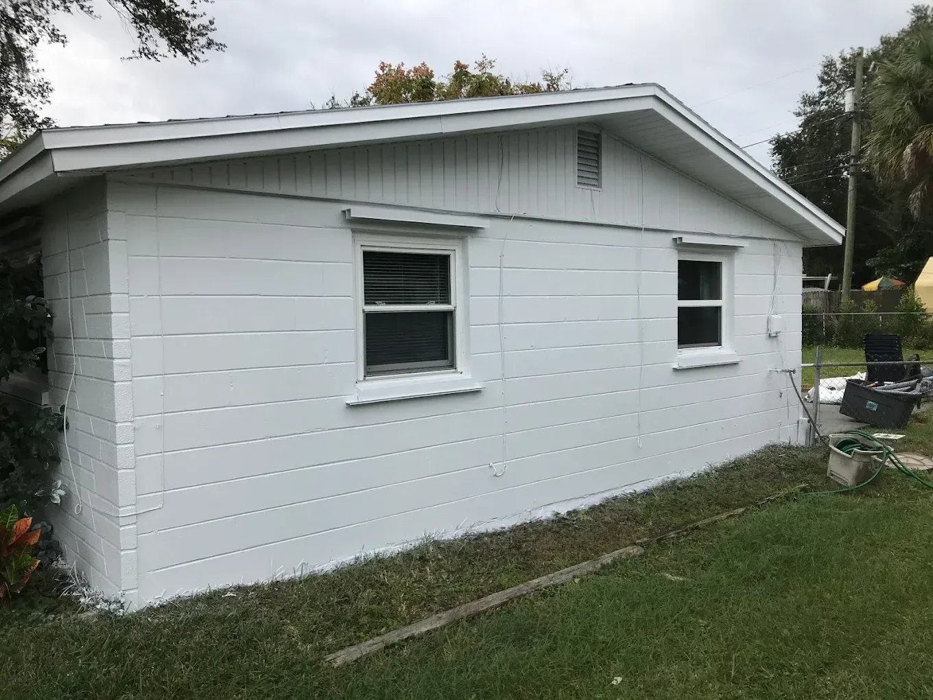 White-painted building with two windows. Grassy yard, overcast sky.
