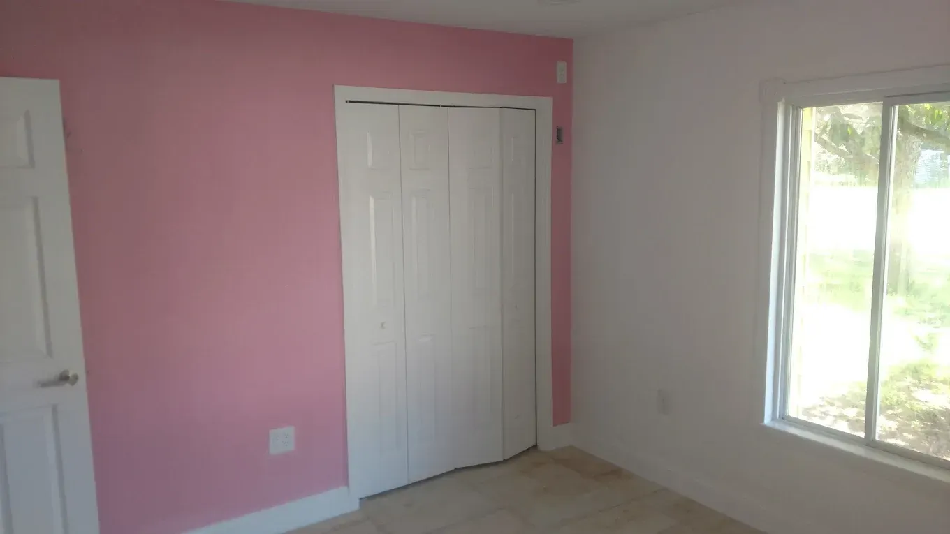 Pink and white painted bedroom interior with a closed closet door and a window.