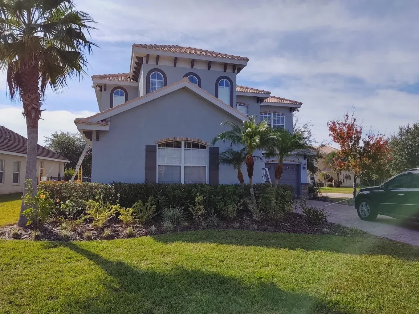 Two-story house with blue stucco walls, brown shutters, and a clay tile roof. A palm tree is visible.
