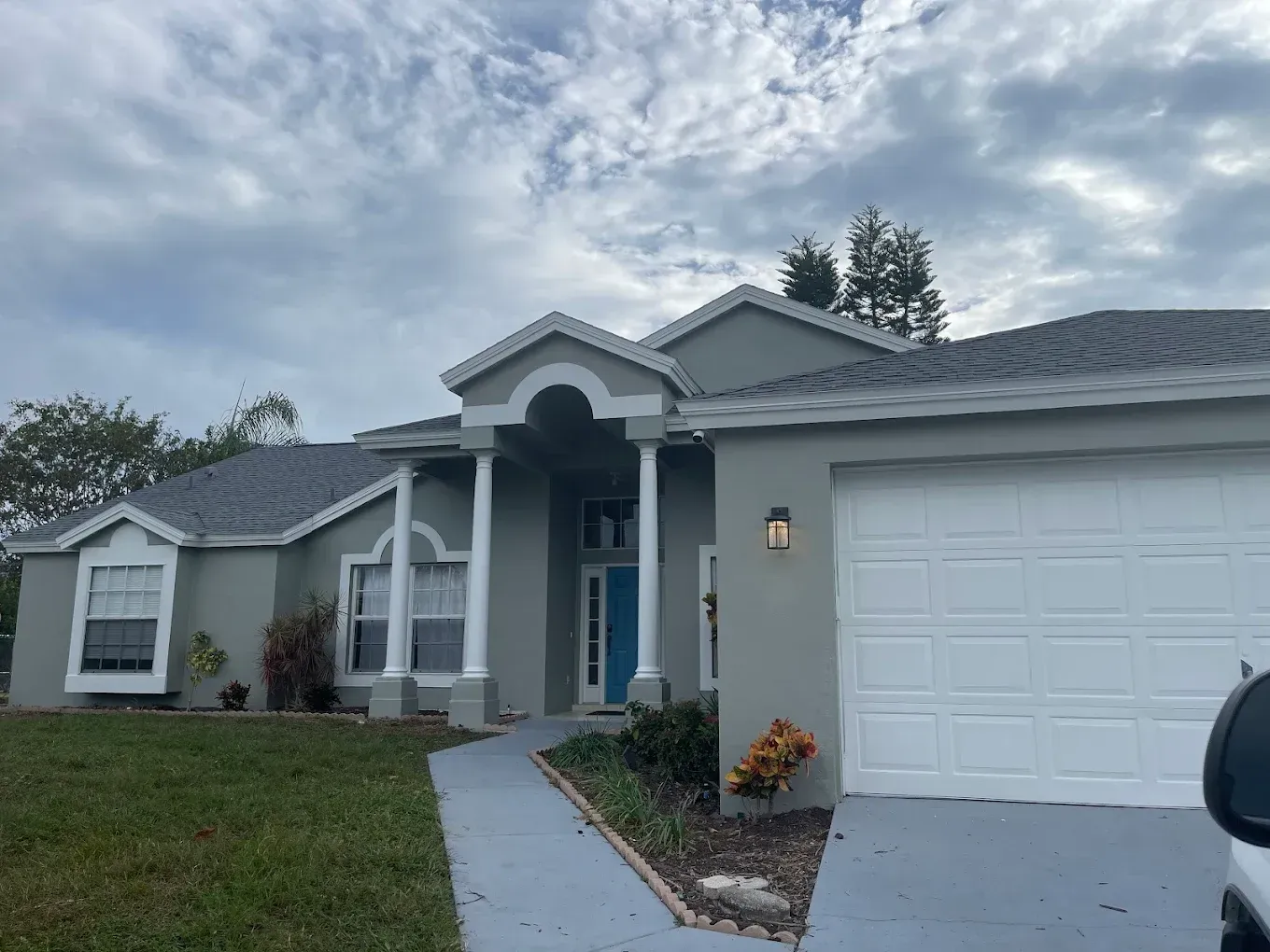 Gray house with white garage door and teal front door, cloudy sky.