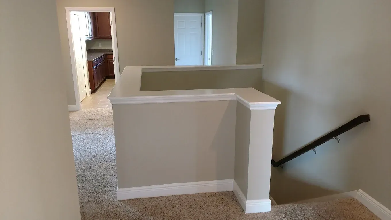 Hallway with tan walls, carpet, and a railing with stairs leading down.
