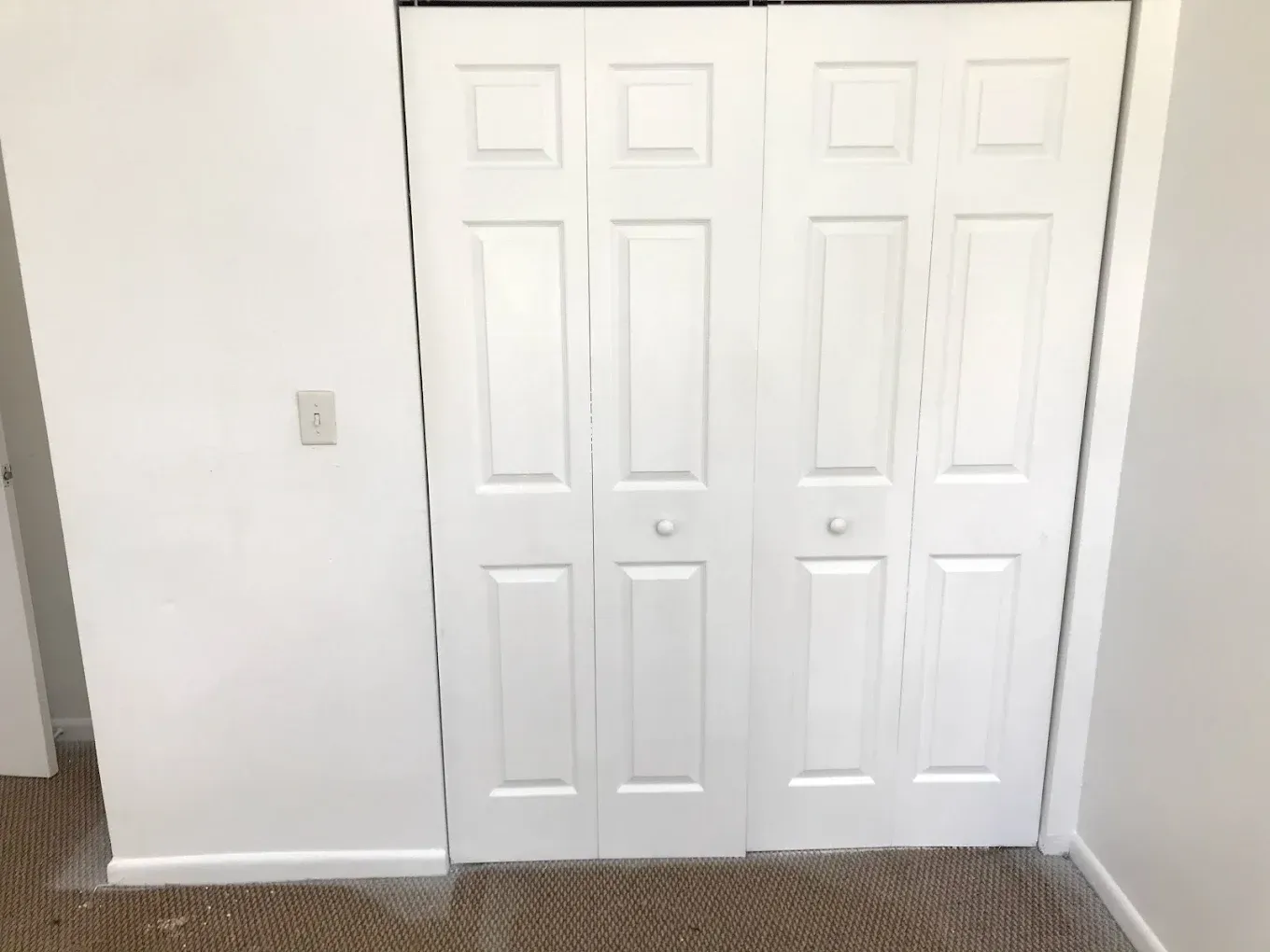 White bi-fold closet doors in a room with a light-colored carpet and walls.