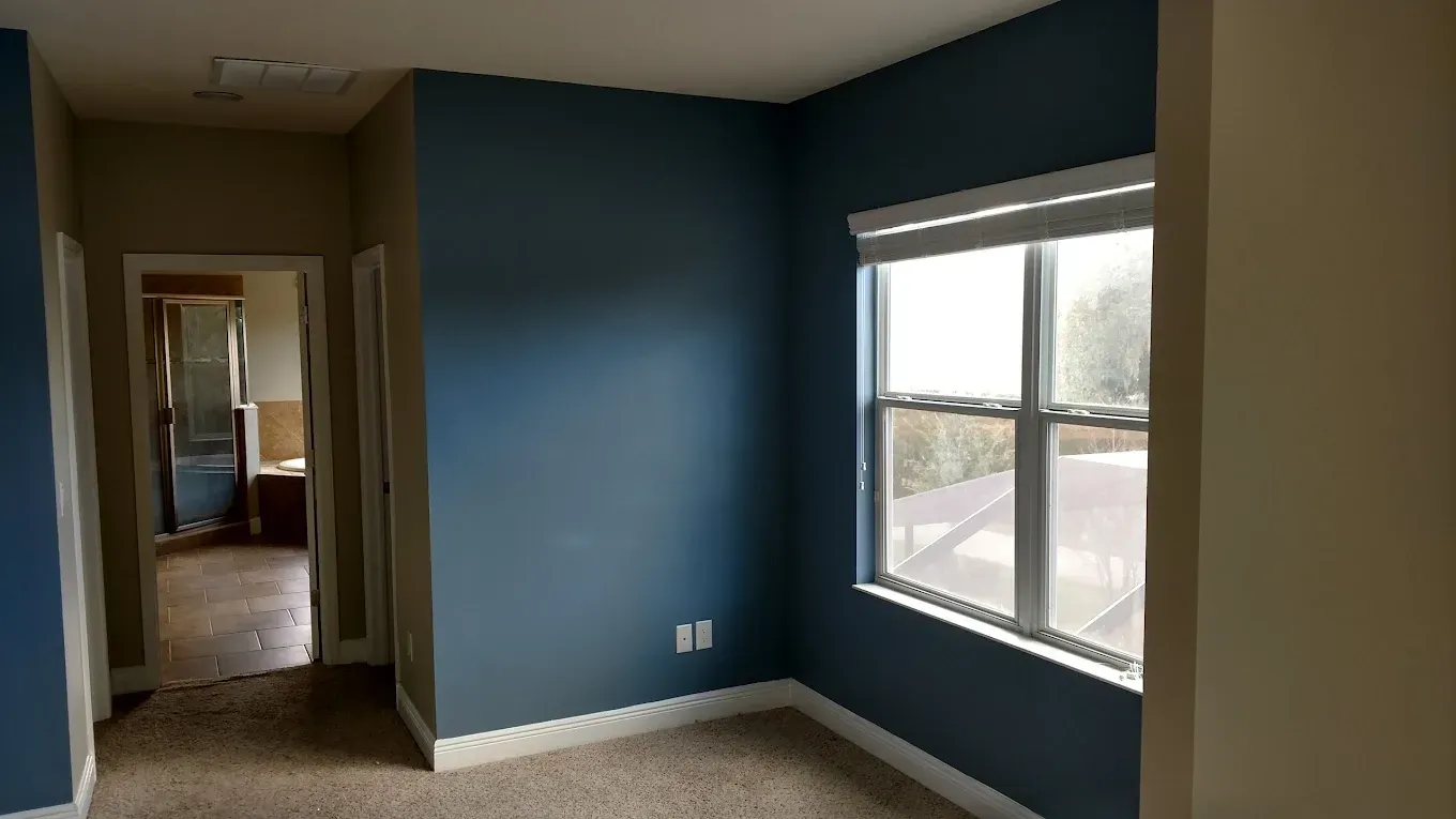 Empty room with blue accent wall, window, and doorway to another room.