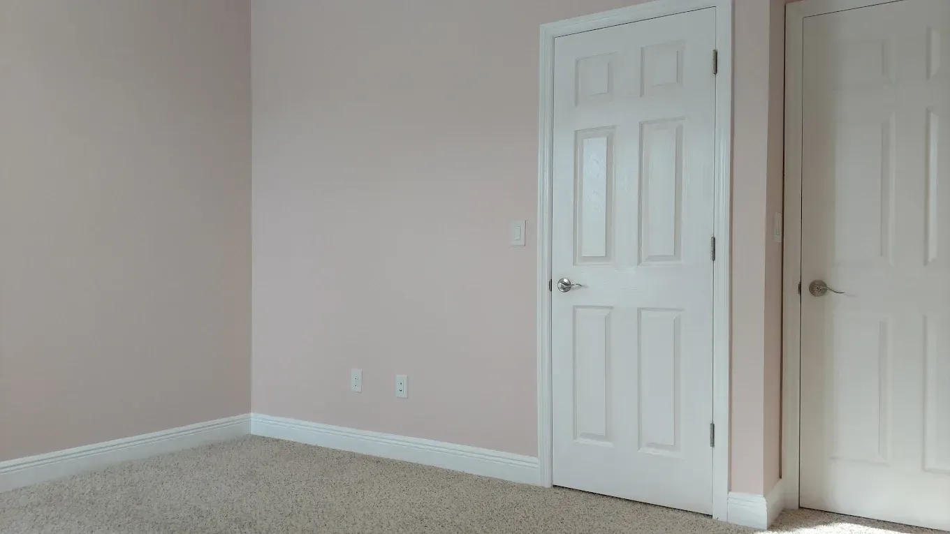 Empty room with pink walls, white doors, and beige carpet.