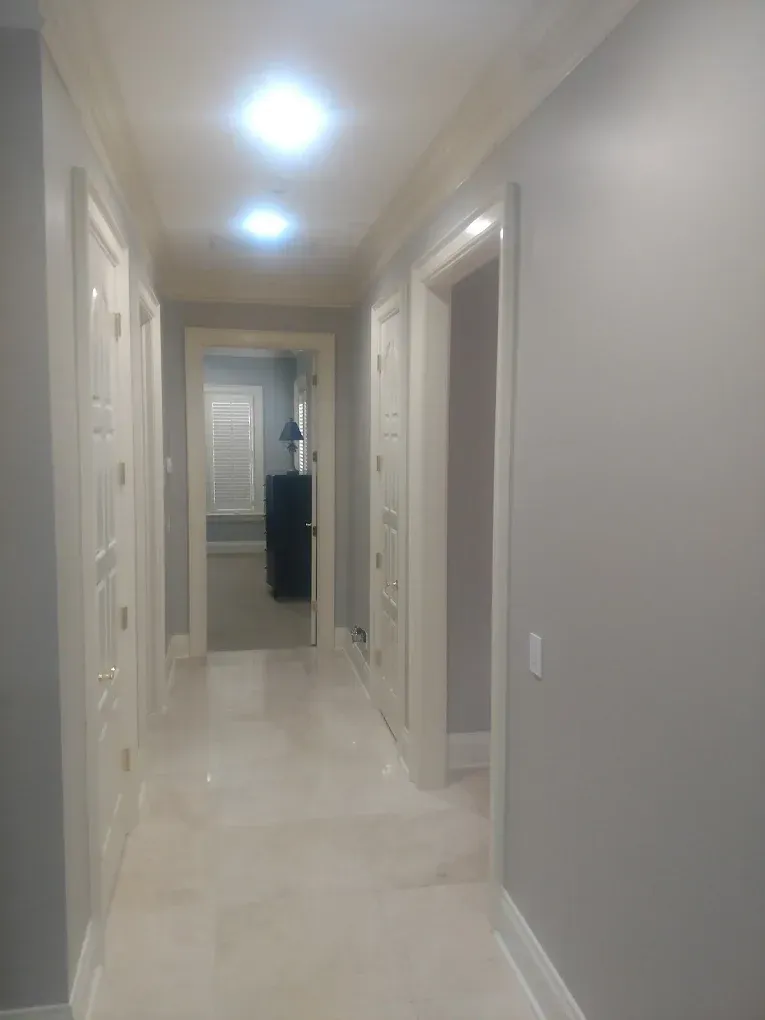 Long hallway with white doors, light gray walls, and bright overhead lights.