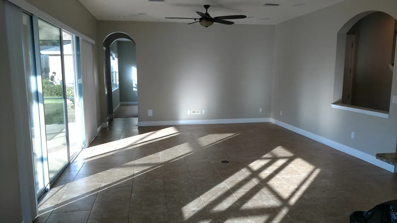 Empty living room with tan tile floor, sliding glass doors, and arched doorways, light streaming in.