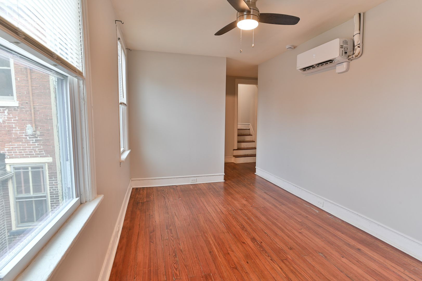 Empty room with hardwood floors, two windows, and an air conditioning unit.