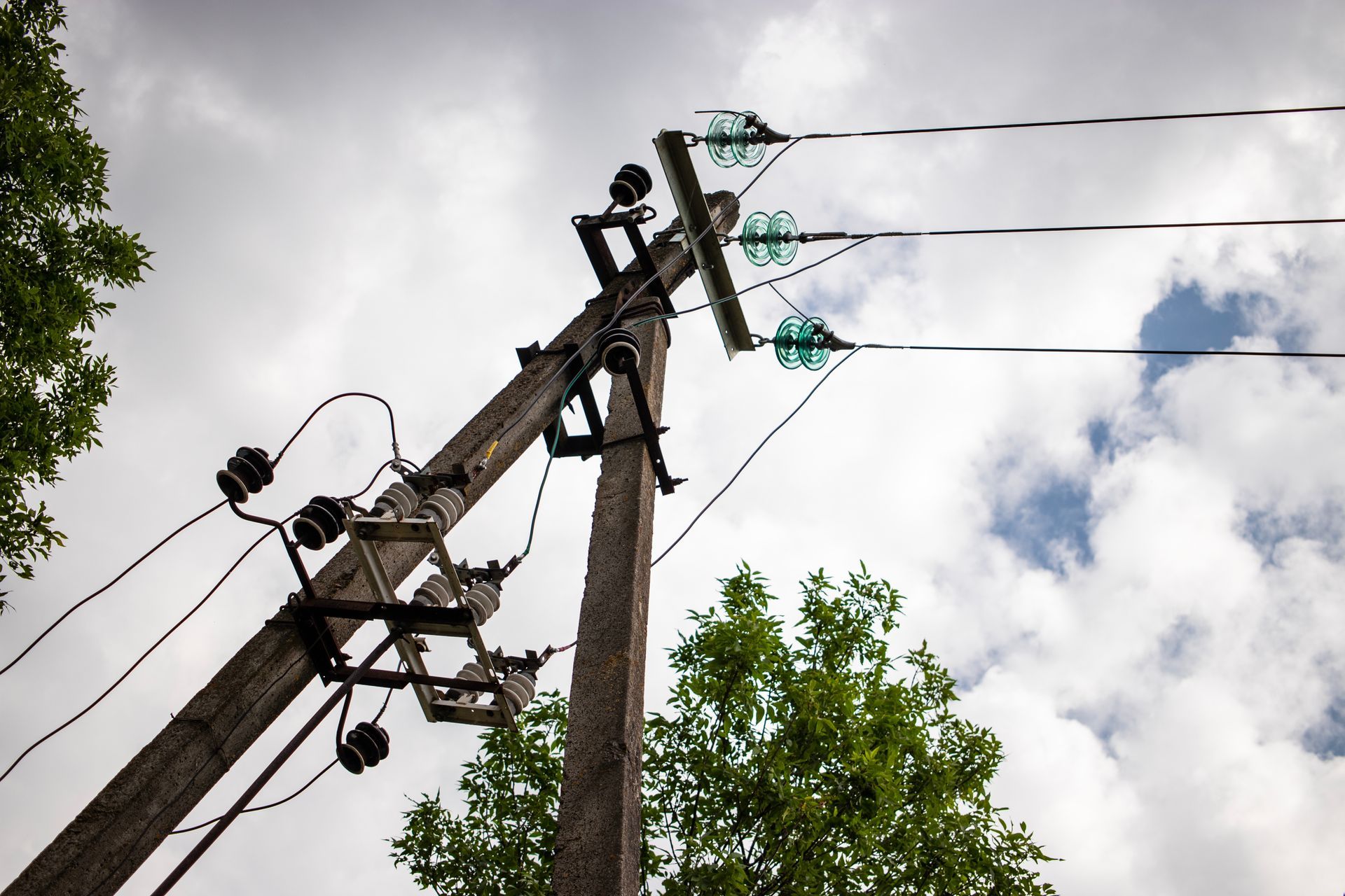 Wooden utility pole with electrical wires and glass insulators against a cloudy sky.