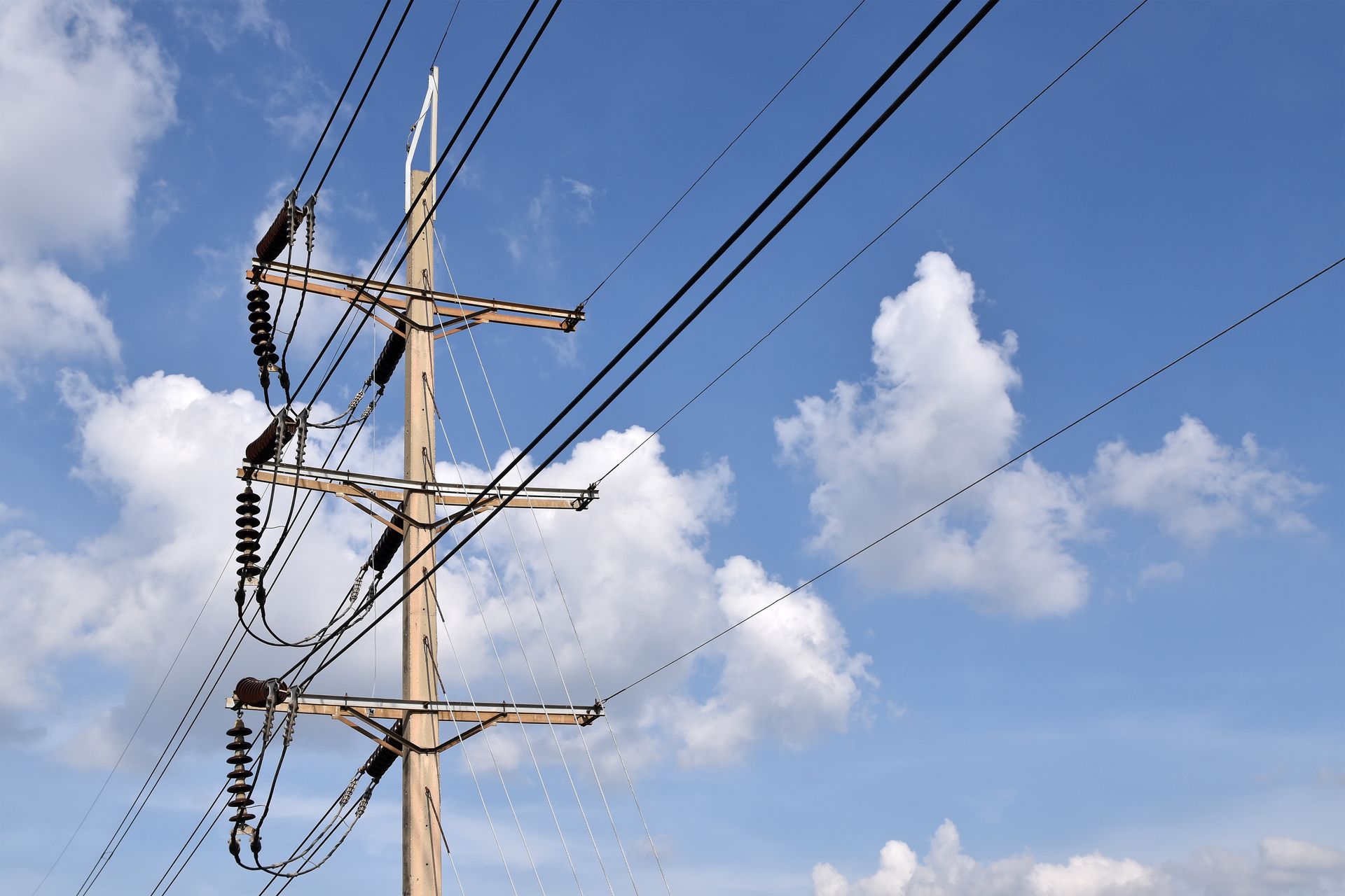 Power lines and pole against a blue sky with fluffy white clouds.